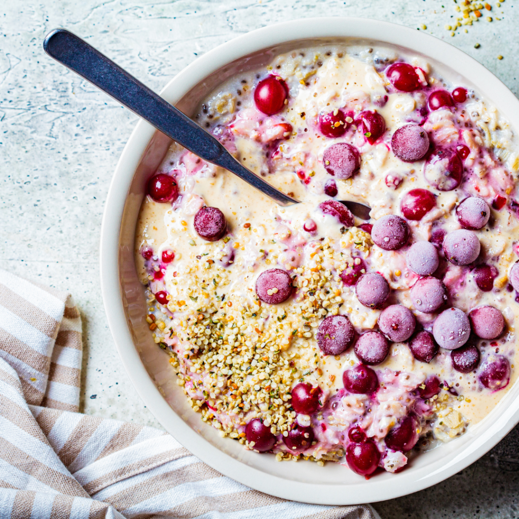 Smoothie bowl with cranberries and a sprinkle of hemp seeds on a marble worktop with a spoon in the bowl and a towel beside