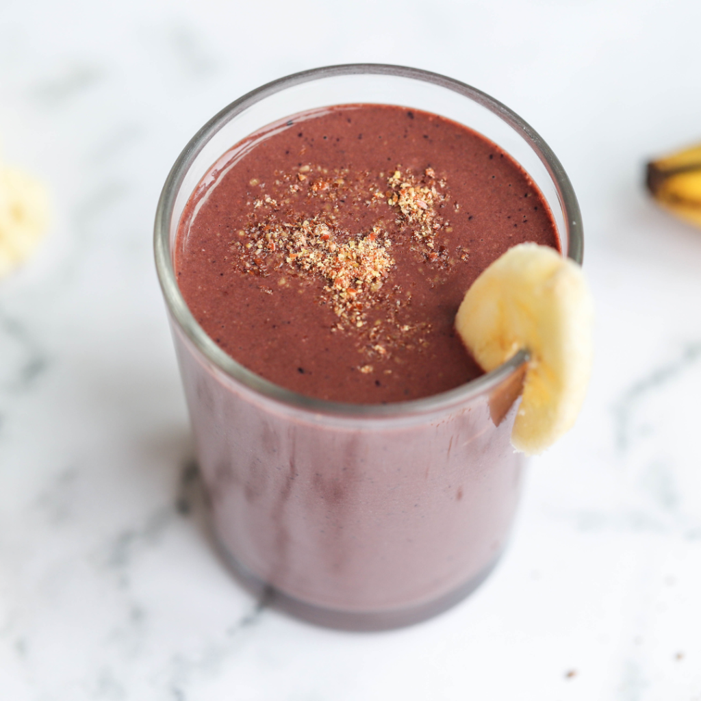 A superfood protein smoothie with a piece of banana decorating it on a white marble top with bananas to the side.