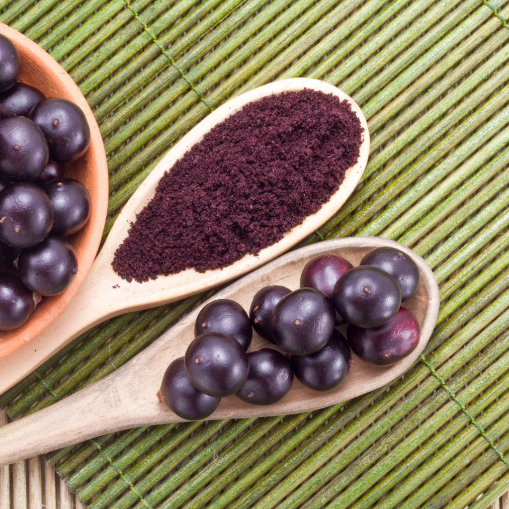 Acai berries and powder on wooden spoons on a bamboo mat